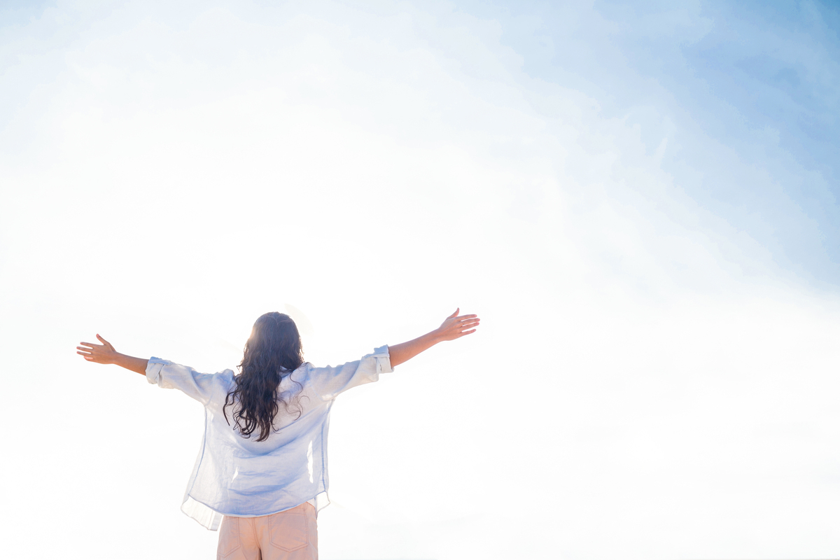 Happy woman with arms outstretched at the beach on a sunny day - オーガニック素材を使用した無添加の2960グラノーラ